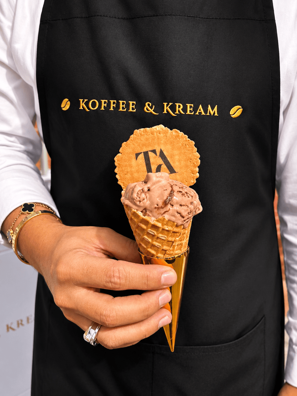 A server wearing a black koffee and kream apron holding a cone of bueno gelato