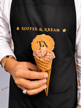 A server wearing a black koffee and kream apron holding a cone of bueno gelato